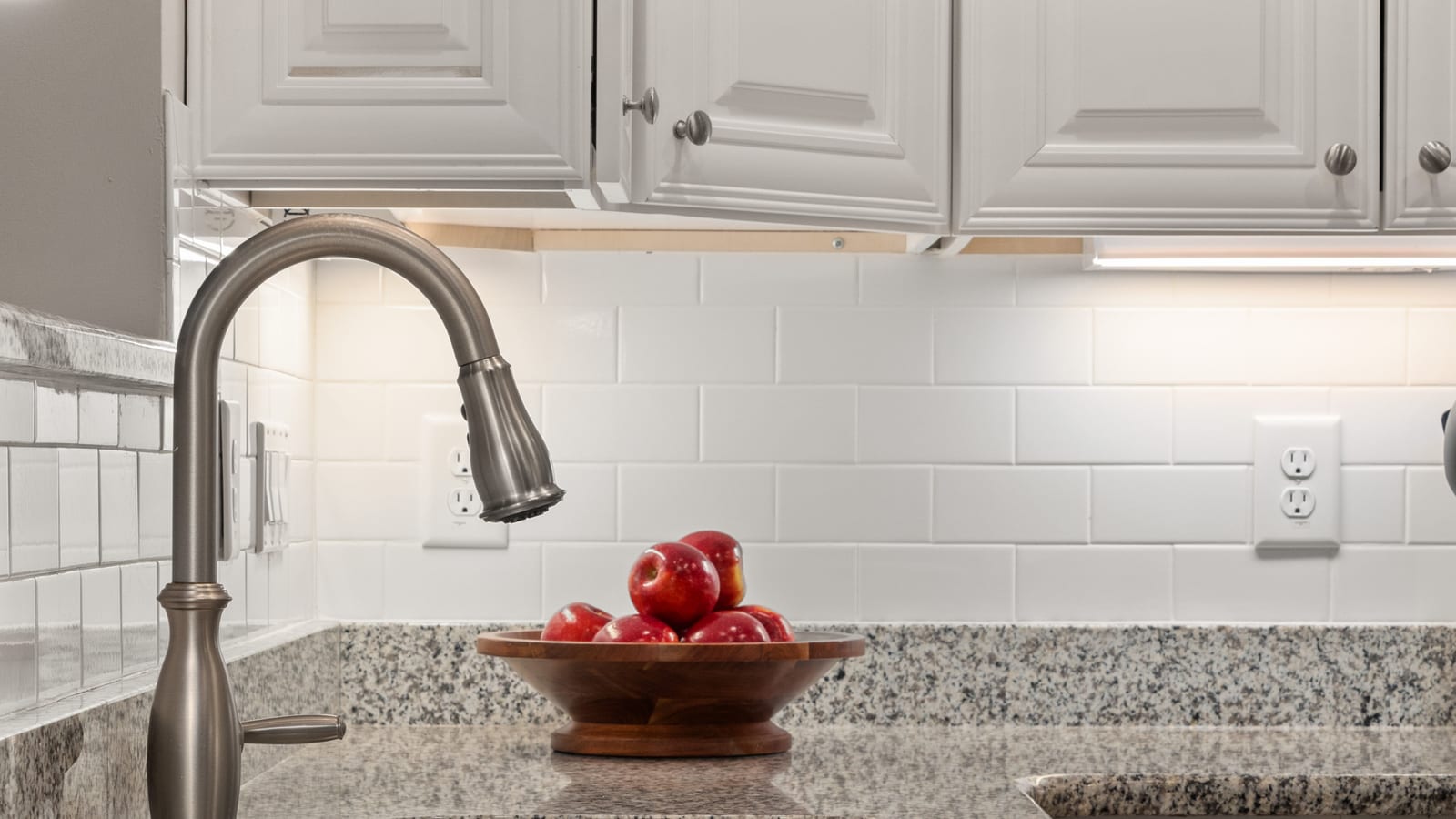 Elegant kitchen countertop featuring fresh apples in a wooden bowl beside a sleek stainless steel sink.