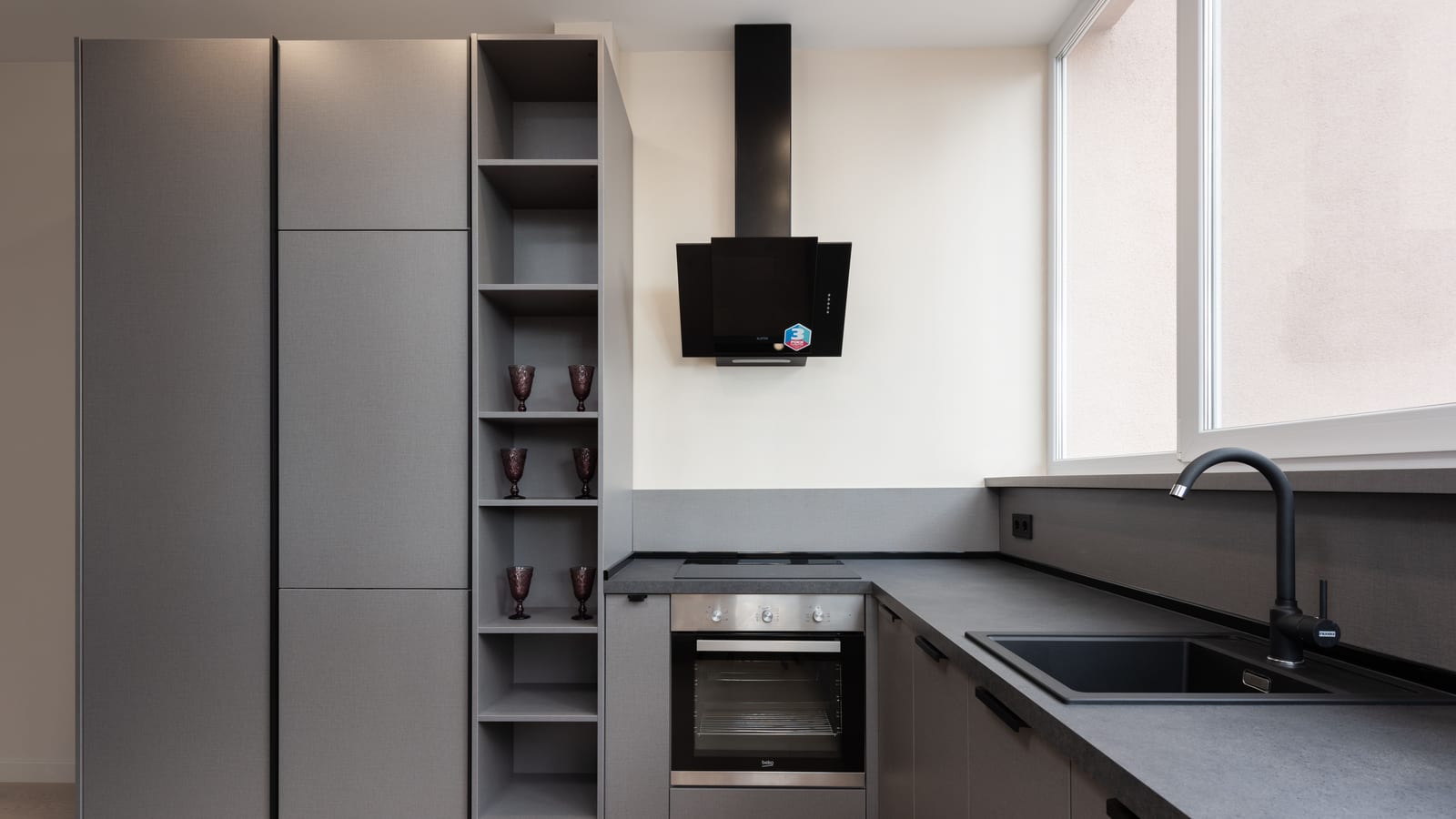 Interior of light gray kitchen corner furnished with cupboards and stone counter with built in oven and sink placed with big windows in apartment