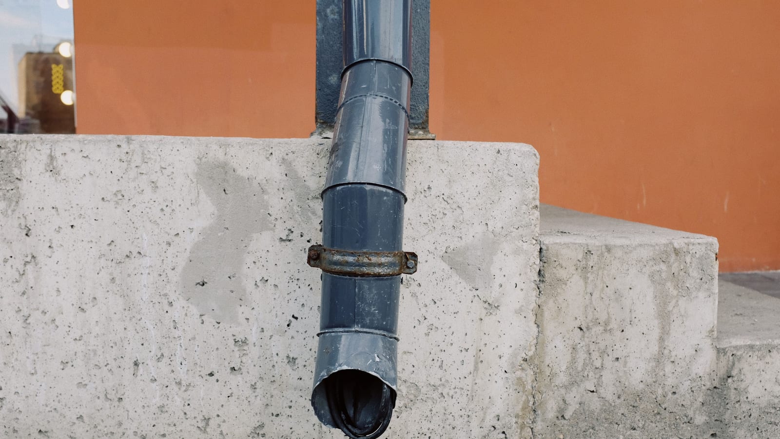 Aged metal drain pipe on a concrete wall with water stains, highlighting urban decay.
