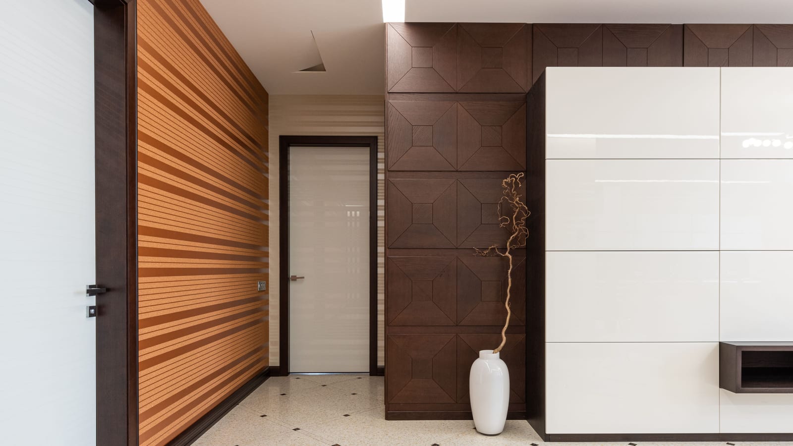 Interior of spacious hallway of modern apartment with door and white vase placed at wall on tiled floor at home