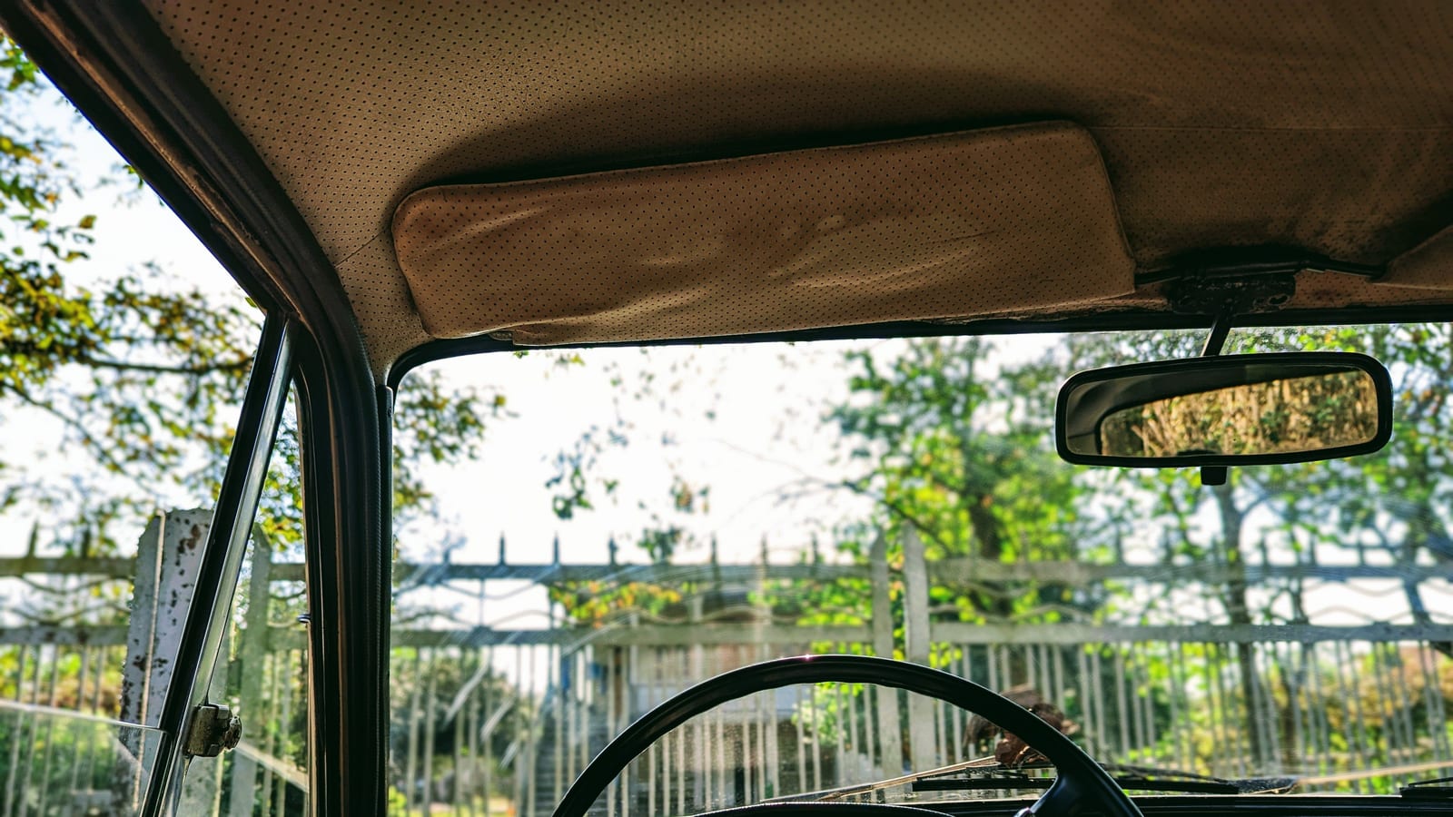 View through the windshield of a vintage car with sunlight streaming in, showcasing the dashboard and steering wheel.