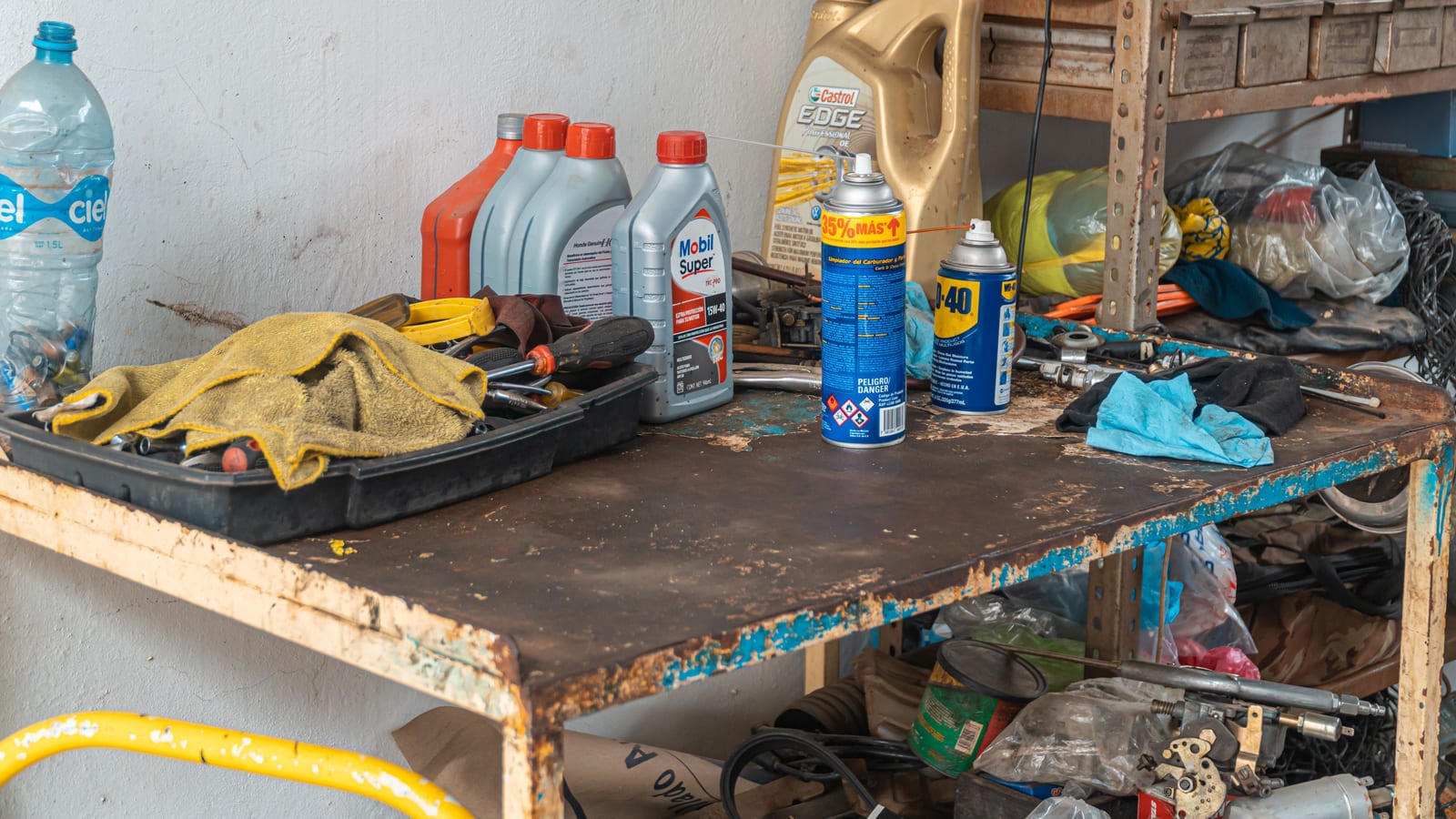 A cluttered workbench in an automobile garage with tools, oil cans, and maintenance products.